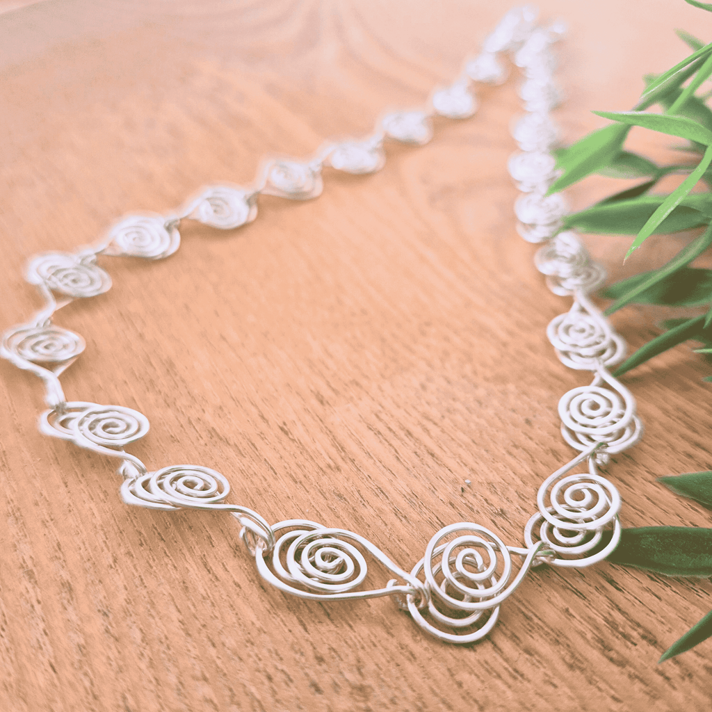Silver wire necklace on a wooden surface with green leaves