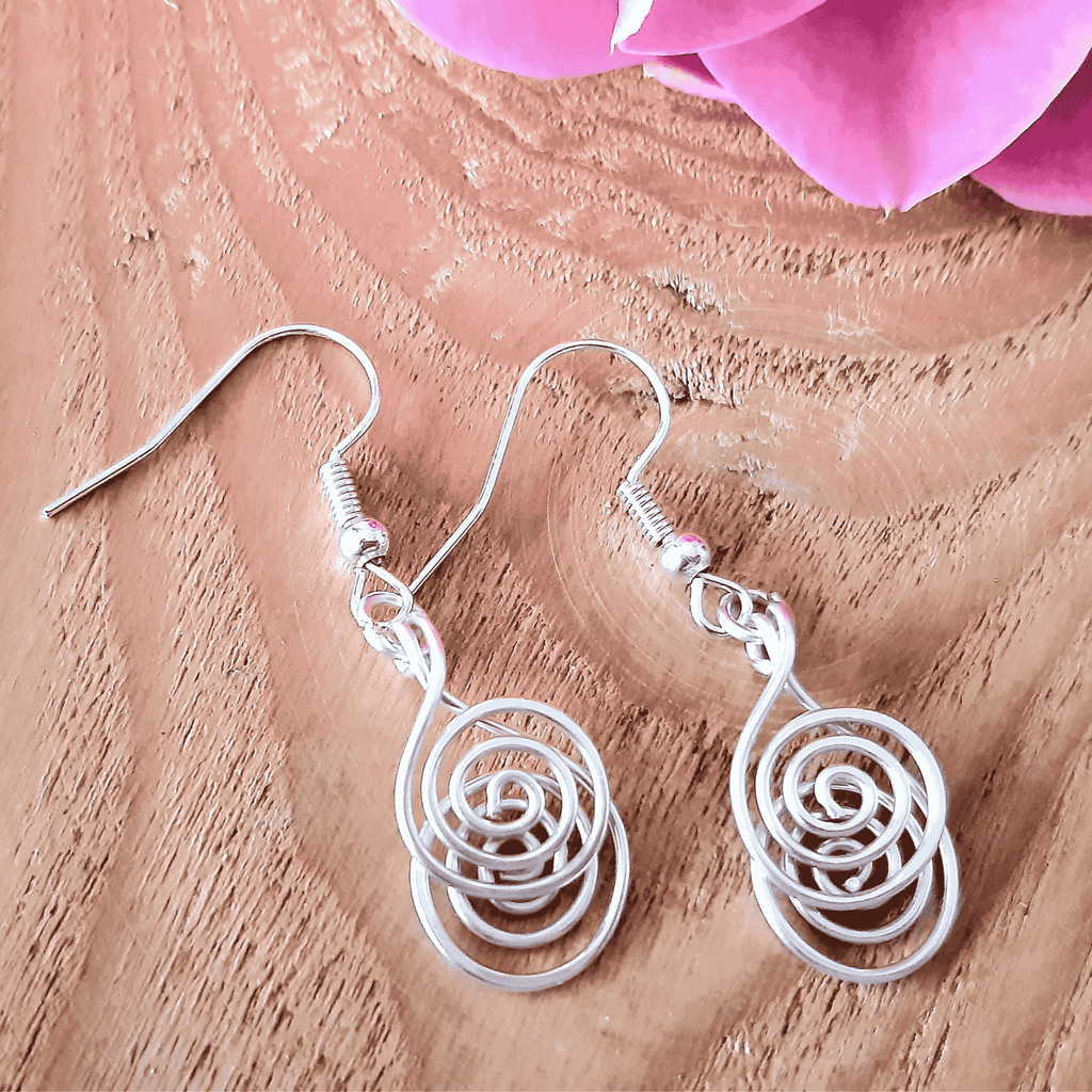 Silver spiral earrings on a wooden surface with pink flowers in the background