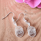 Silver spiral earrings on a wooden surface with pink flowers in the background