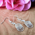 Silver spiral earrings on a wooden surface with pink flowers in the background