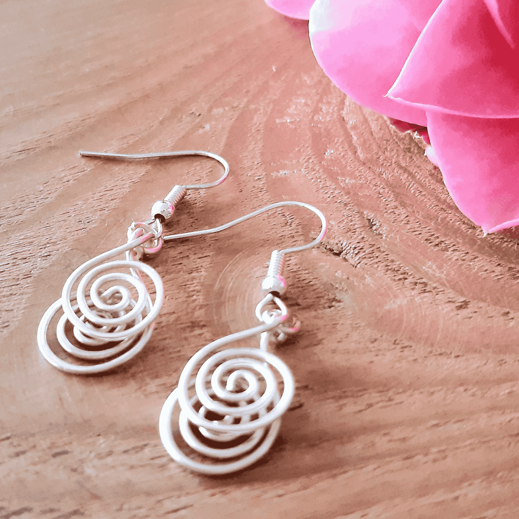 White spiral earrings on a wooden surface with pink fabric in the background