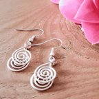 White spiral earrings on a wooden surface with pink fabric in the background