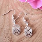 Silver spiral earrings on a wooden surface with pink flowers.
