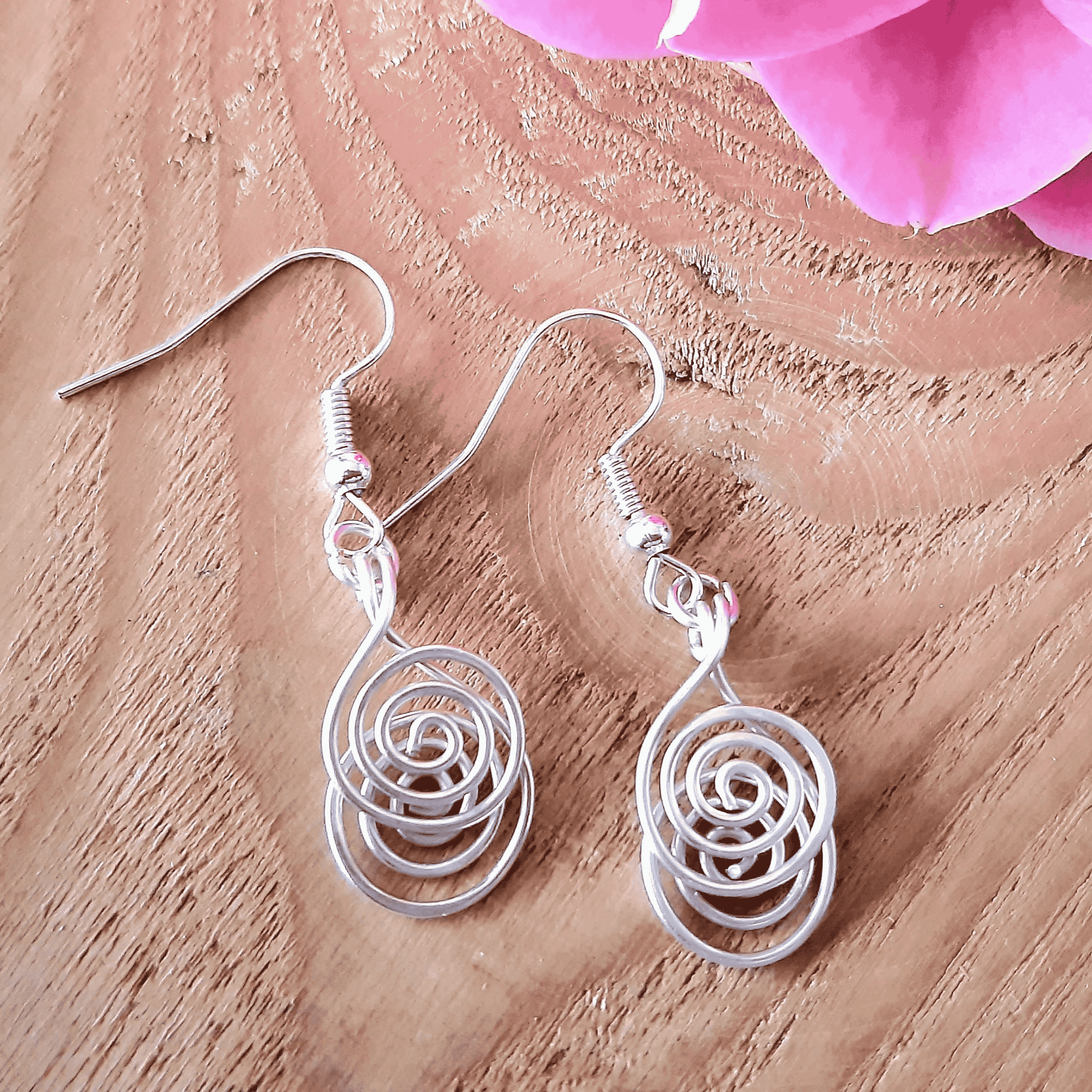 Silver spiral earrings on a wooden surface with pink flowers.