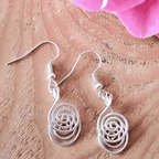 Silver spiral earrings on a wooden surface with pink flowers.