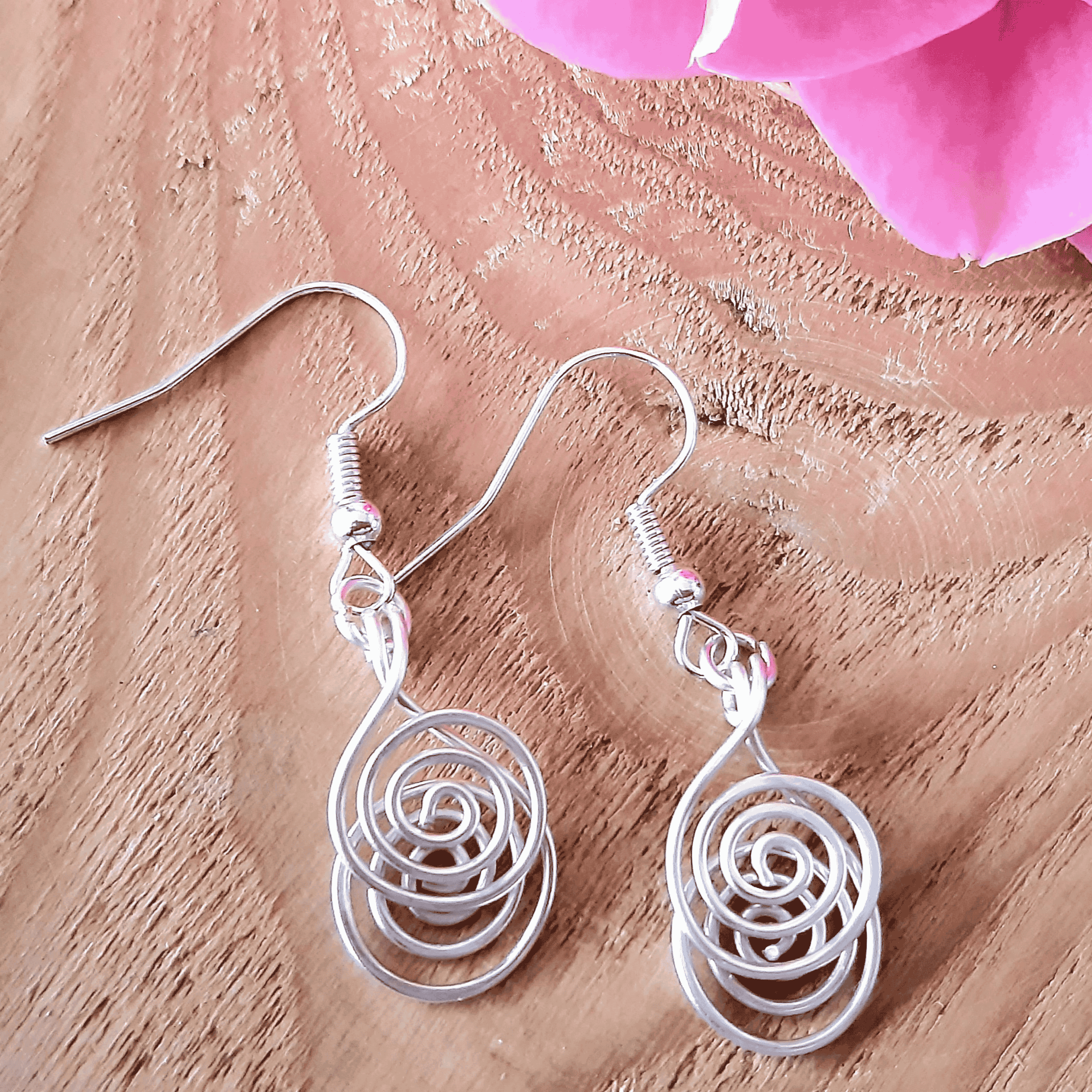 Silver spiral earrings on a wooden surface with pink flowers.