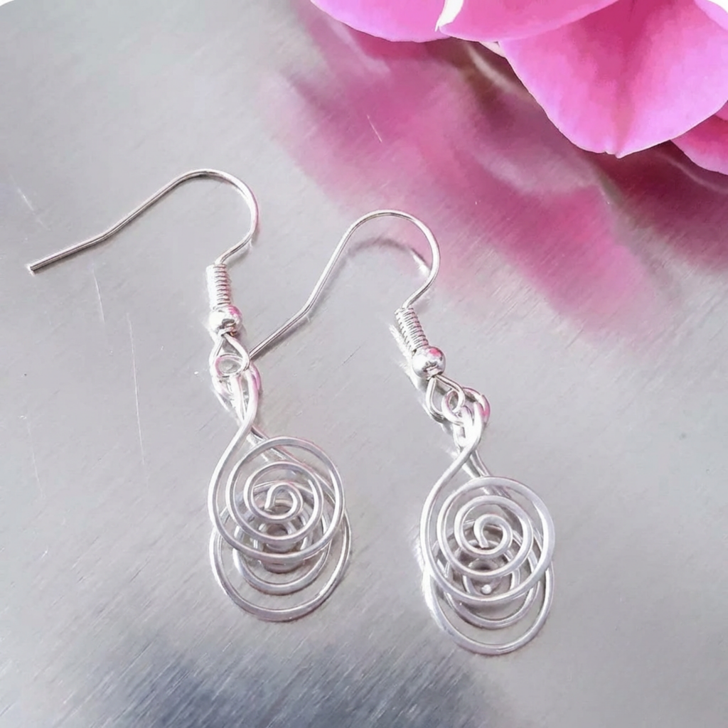 Silver spiral earrings on a metallic surface with pink flowers in the background