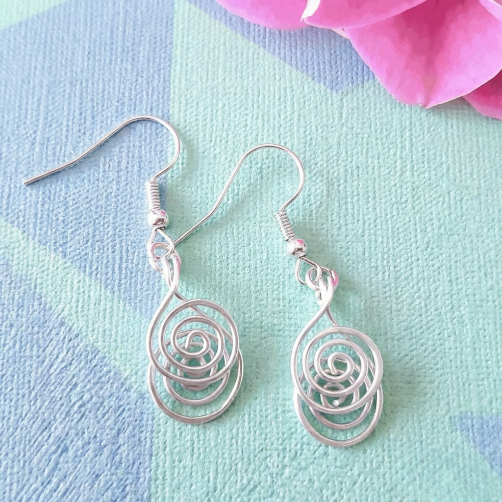 Silver spiral earrings on a colorful fabric background with pink flowers.