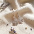 Silver spiral earrings on a textured beige surface with lavender flowers.