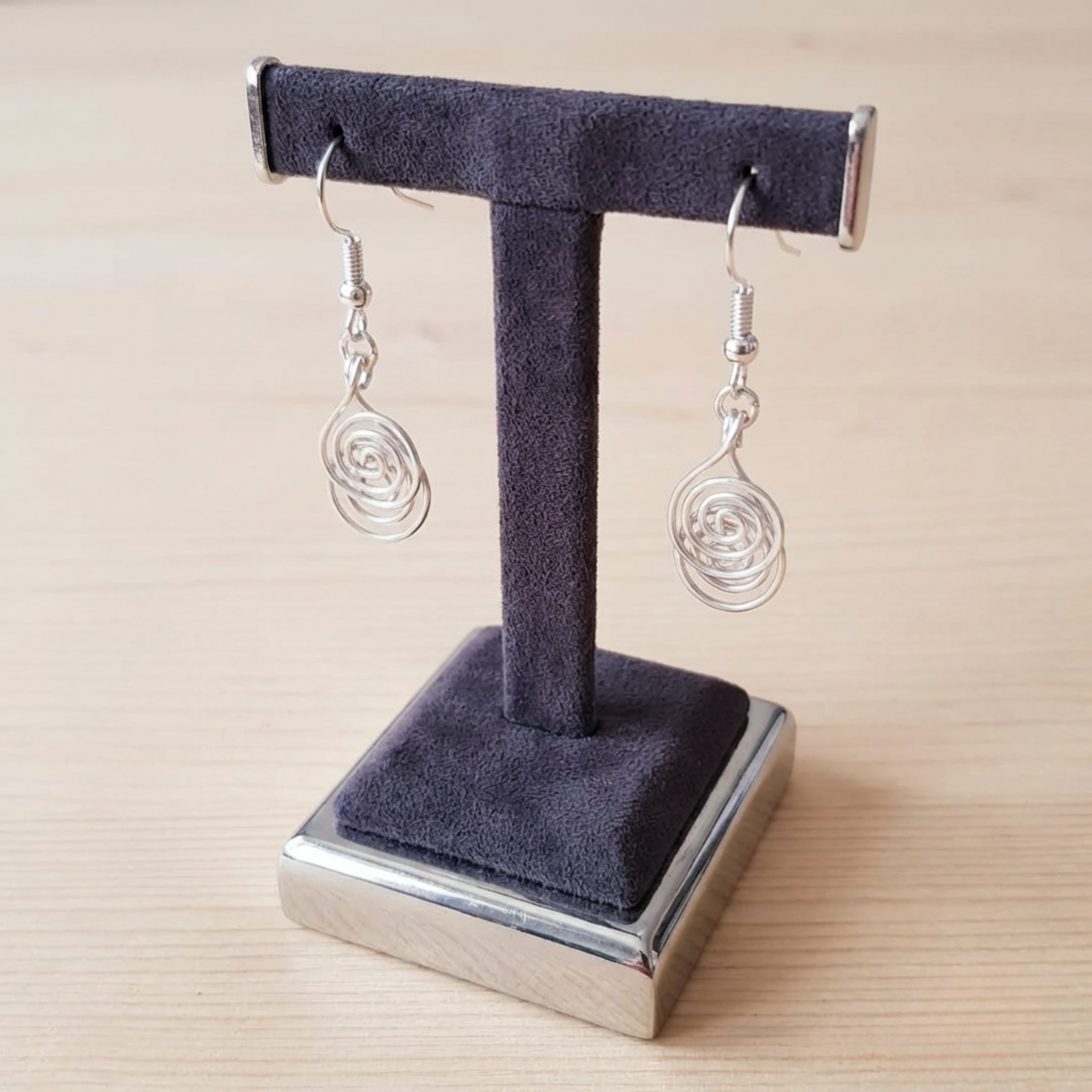 Silver spiral earrings on a dark gray velvet stand with a wooden background