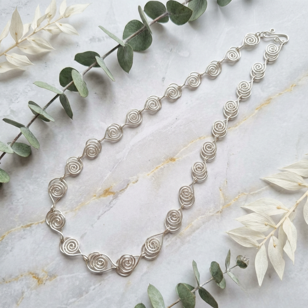 Silver necklace with spiral design on a marble surface with green leaves