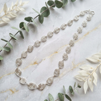 Silver necklace with spiral design on a marble surface with green leaves