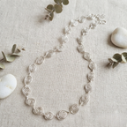 Silver necklace on a textured beige surface with eucalyptus leaves and stones.