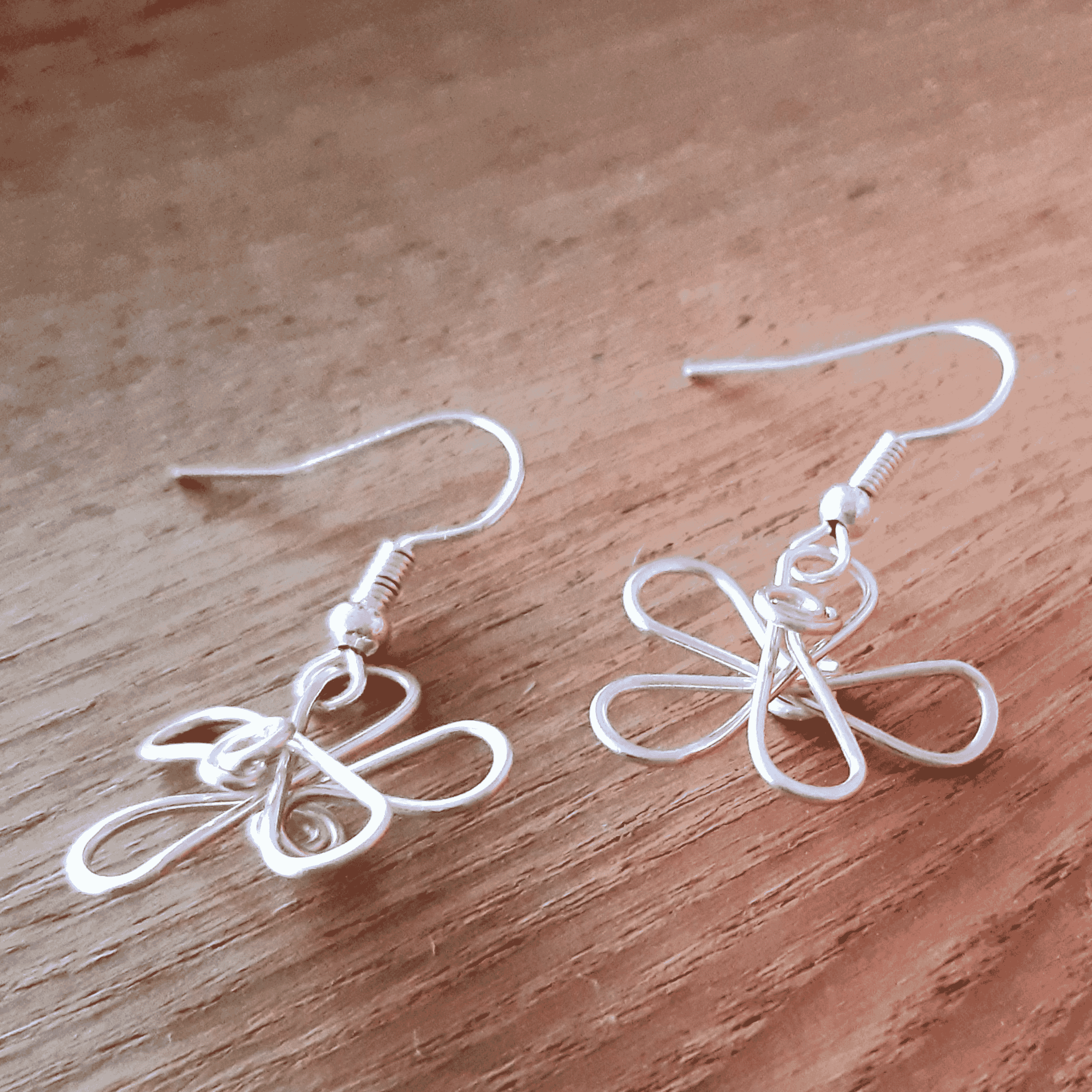 Pair of white wire butterfly earrings on a wooden surface