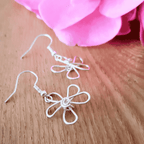 Silver flower-shaped earrings on a wooden surface with pink fabric in the background