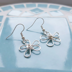 Silver flower-shaped earrings on a blue mosaic tile background