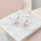 Flower-shaped earrings on a marble surface with a geometric background
