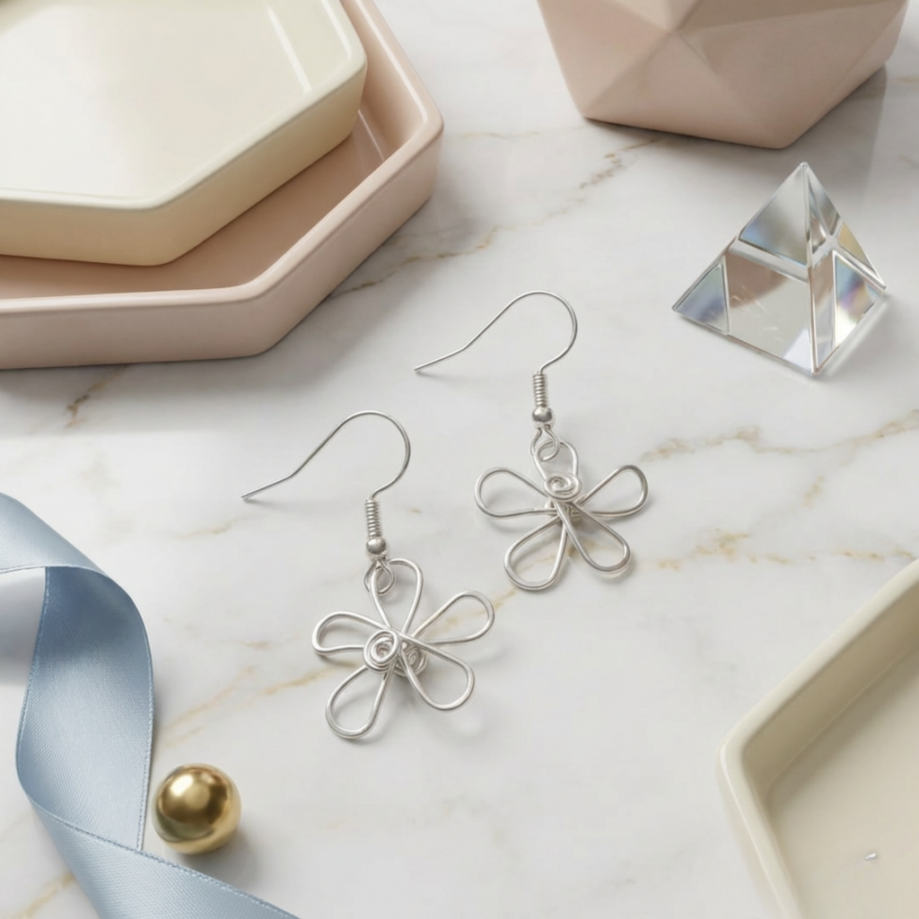 Silver flower earrings on a marble surface with decorative items.