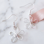 Silver flower-shaped earrings on a marble surface with a pink ribbon.