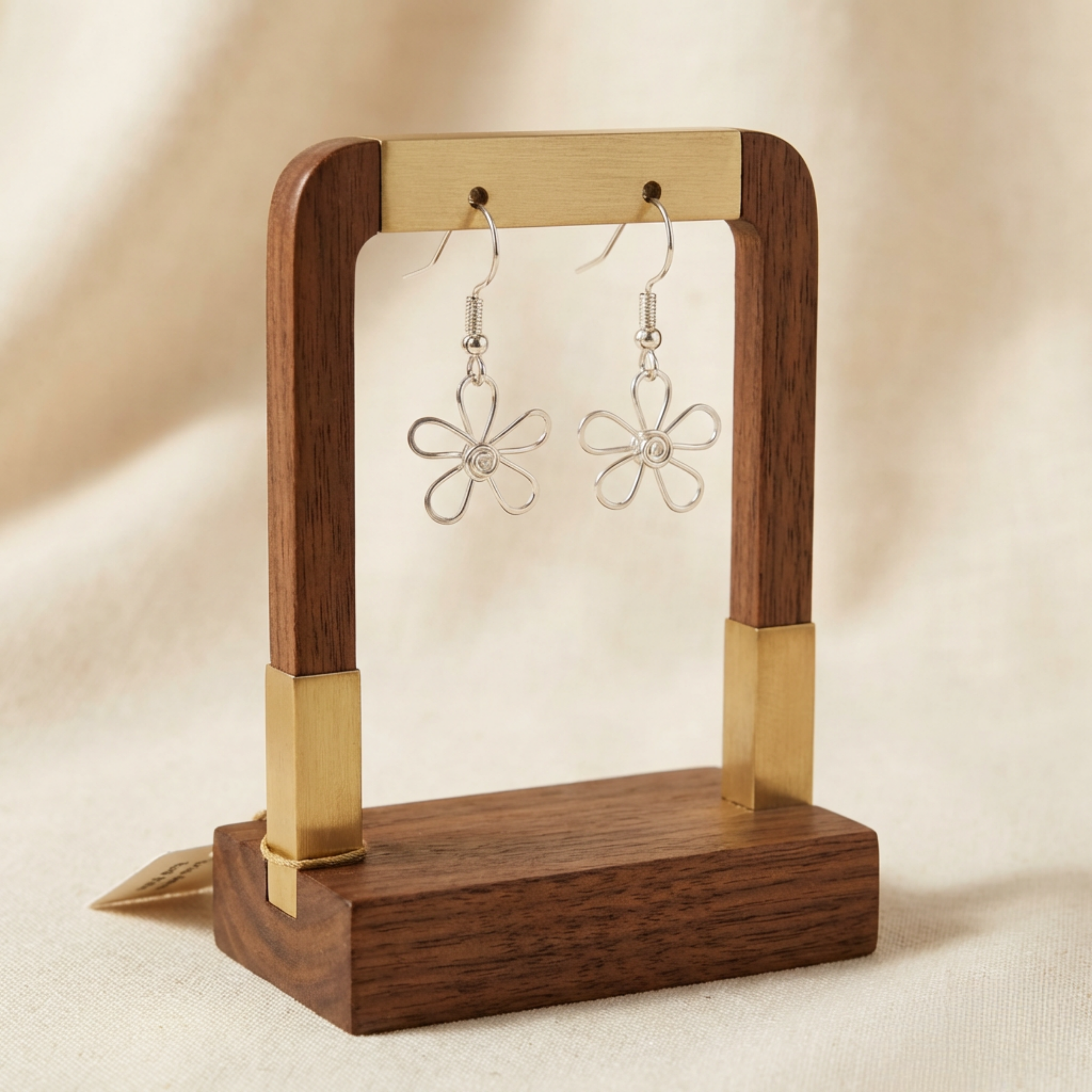 Wooden and brass earring stand with floral earrings on a beige background