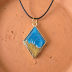 Diamond-shaped pendant with blue and gold design on a brown surface