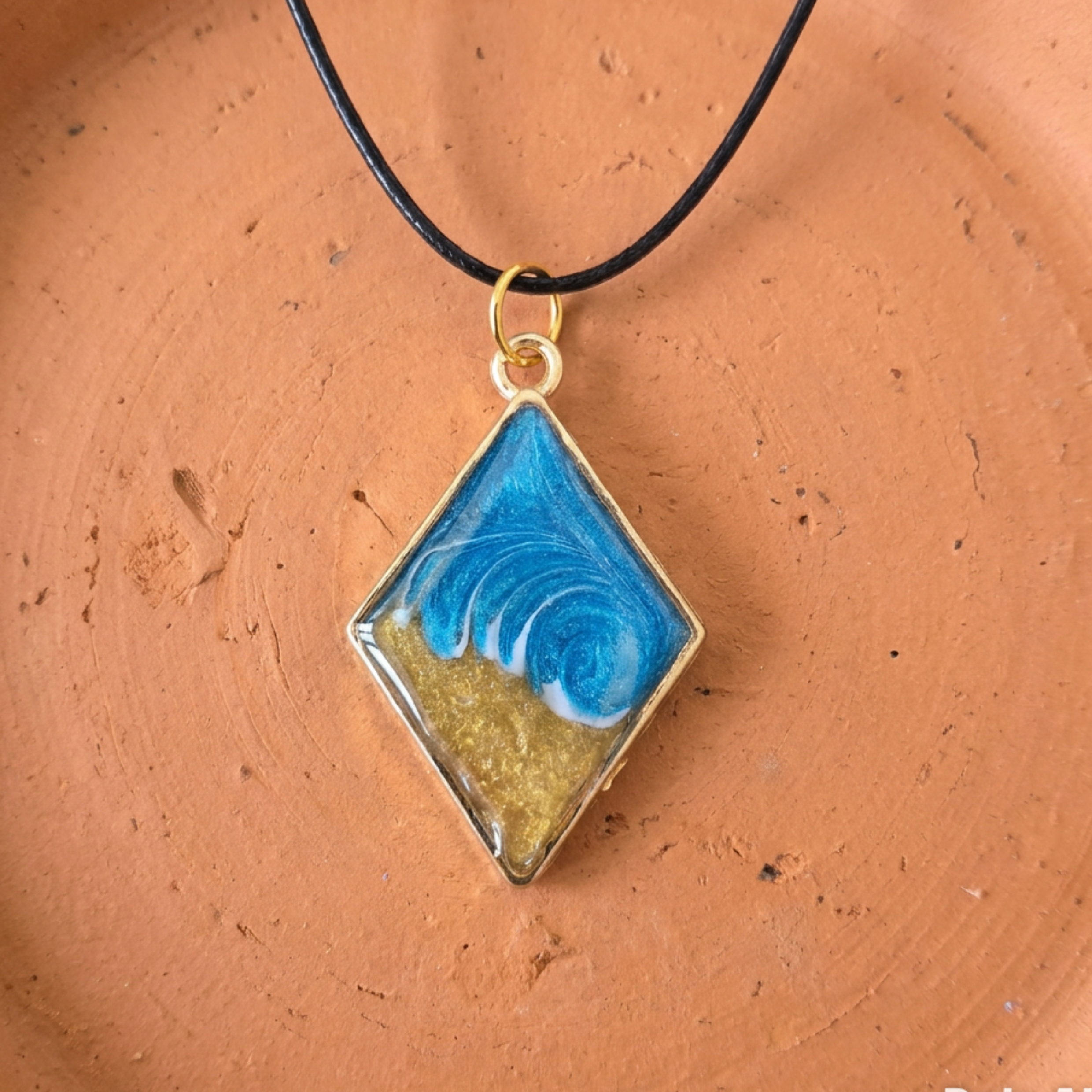 Diamond-shaped pendant with blue and gold design on a brown surface