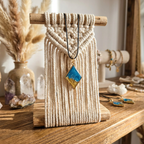 Macrame wall hanging with a pendant on a wooden surface, surrounded by decorative items.