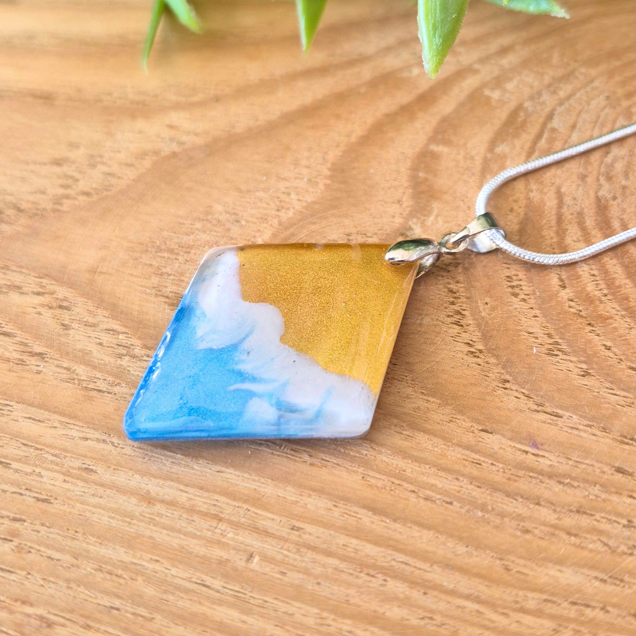 Necklace with a triangular pendant featuring blue, white, and yellow colors on a wooden surface.