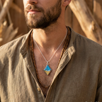 Man wearing a necklace with a blue pendant against a natural background