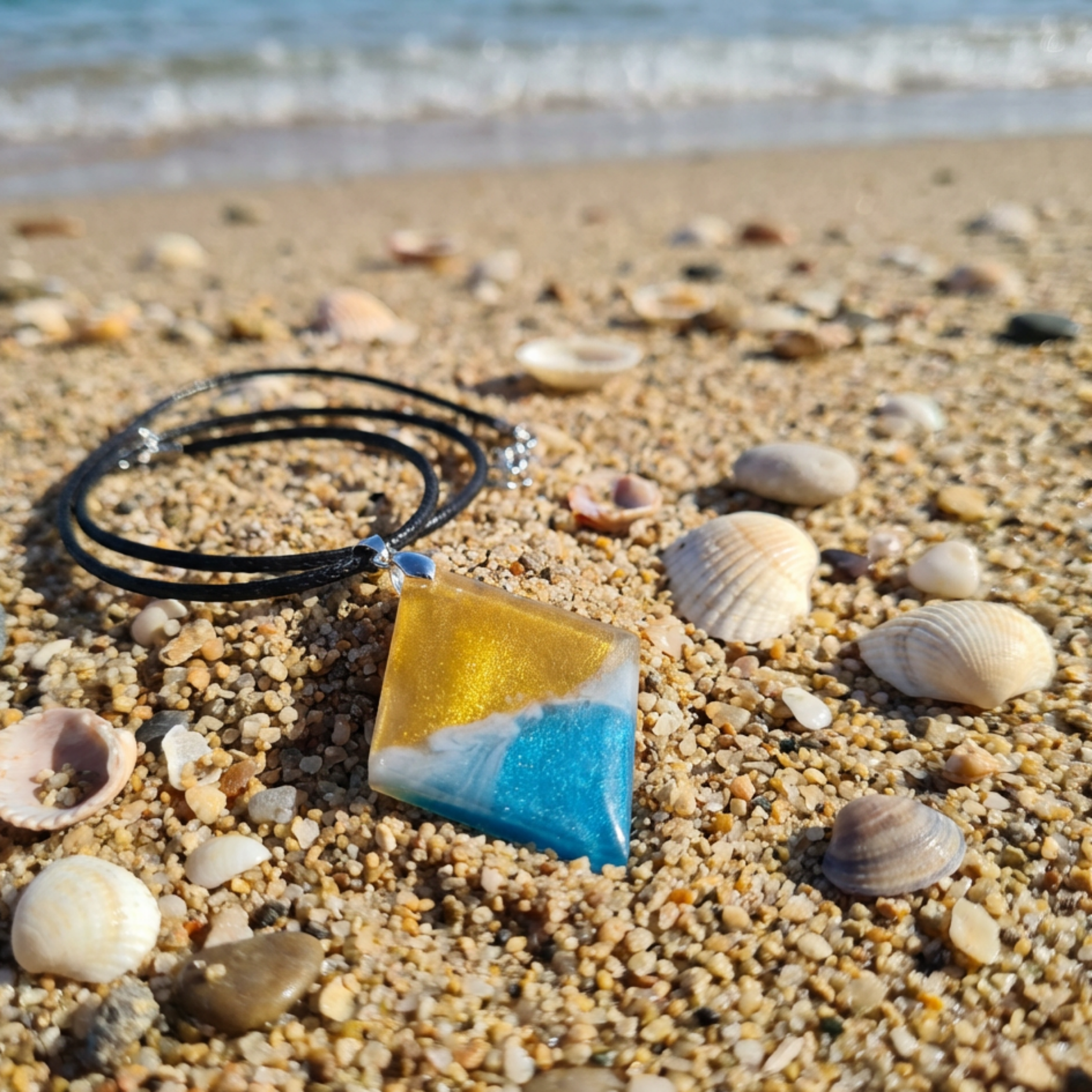 Necklace with a triangular pendant on a sandy beach with shells.