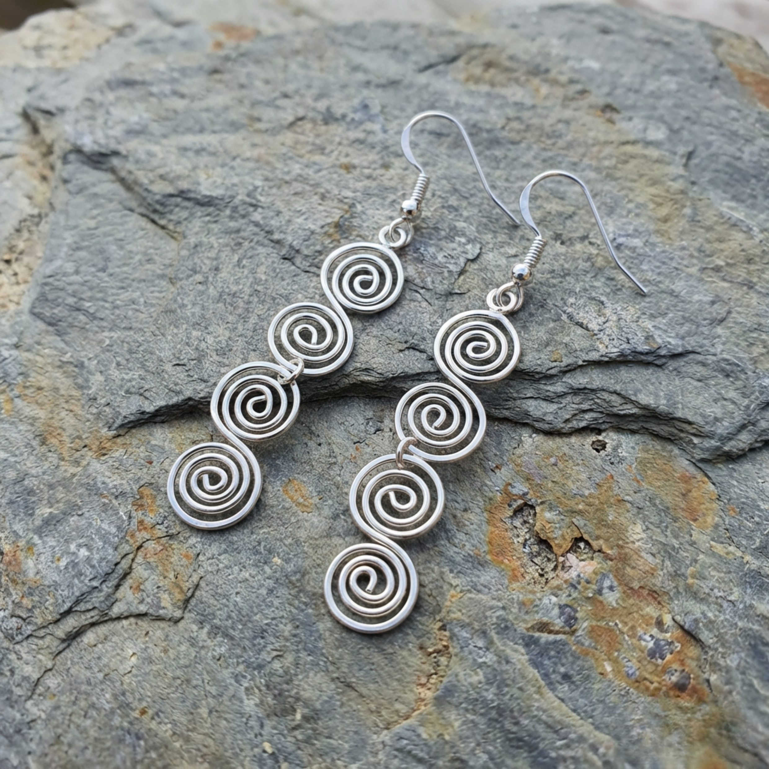 Silver spiral earrings on a stone surface