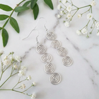 Silver spiral earrings on a marble surface with white flowers and green leaves.