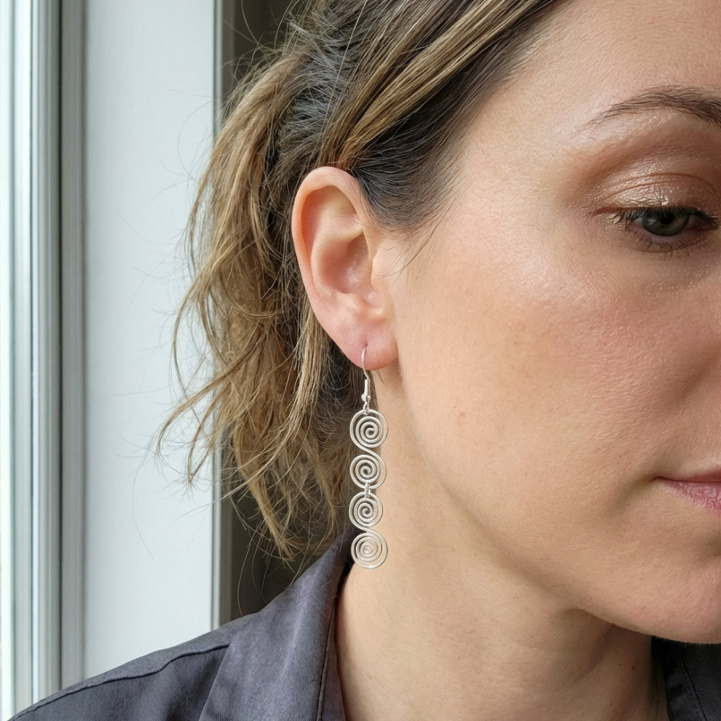 Close-up of a woman wearing silver spiral earrings with a neutral background