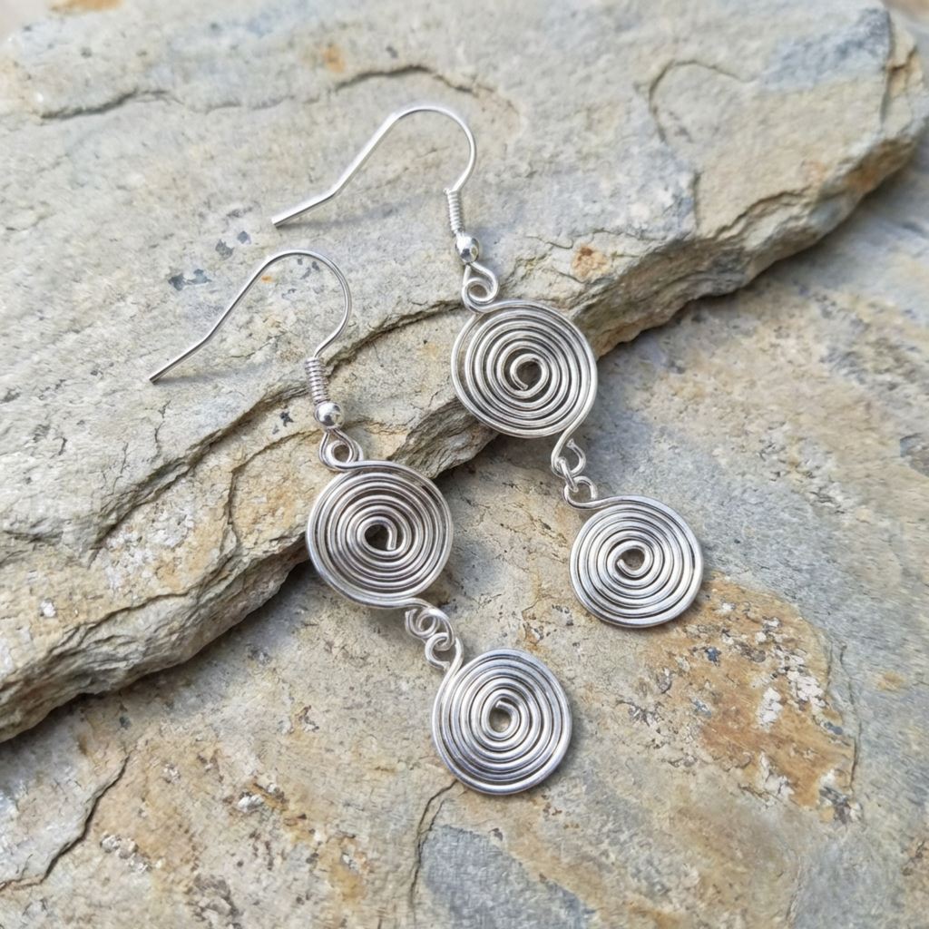 Silver spiral earrings on a stone surface