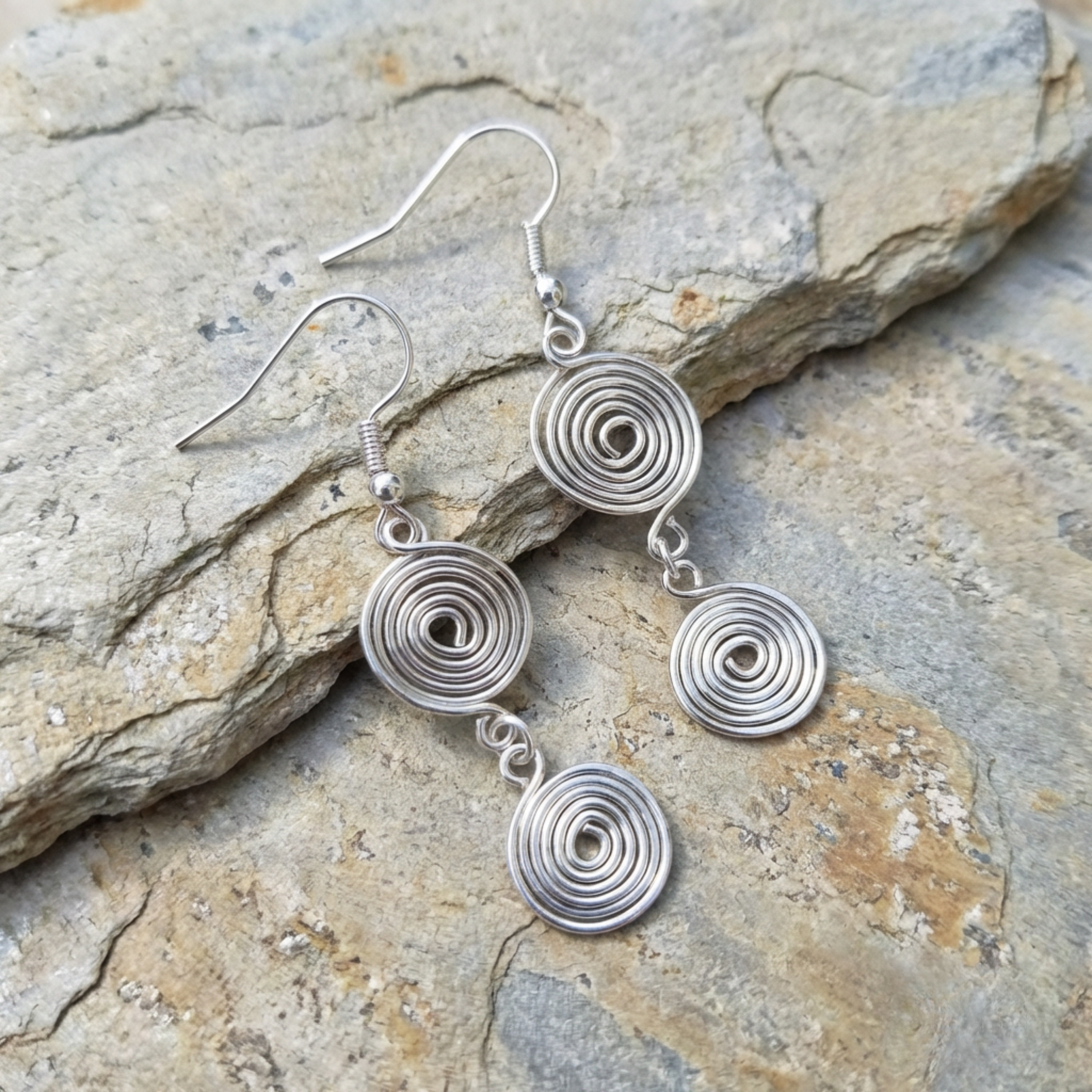 Silver spiral earrings on a stone surface