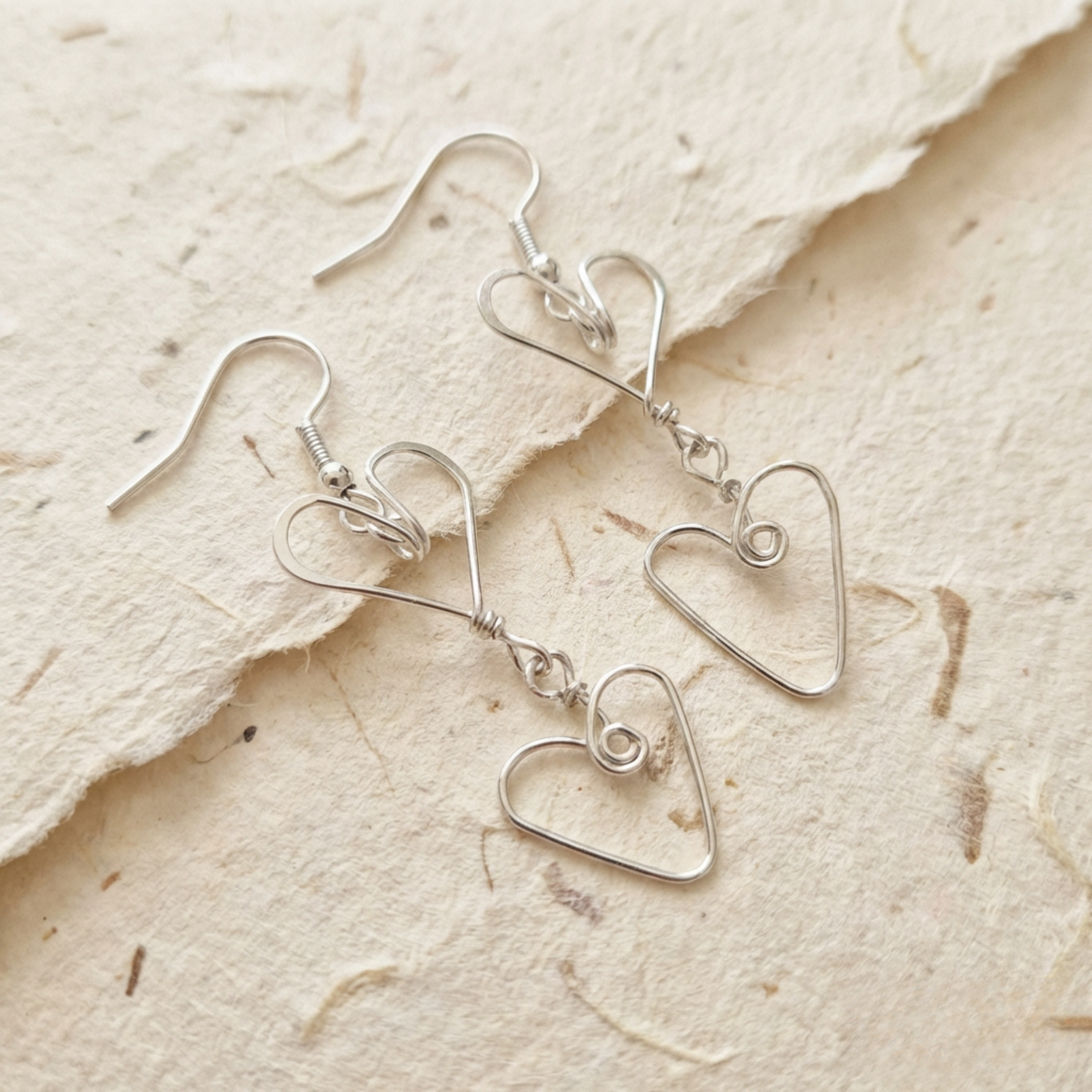 Silver heart-shaped earrings on a textured beige surface