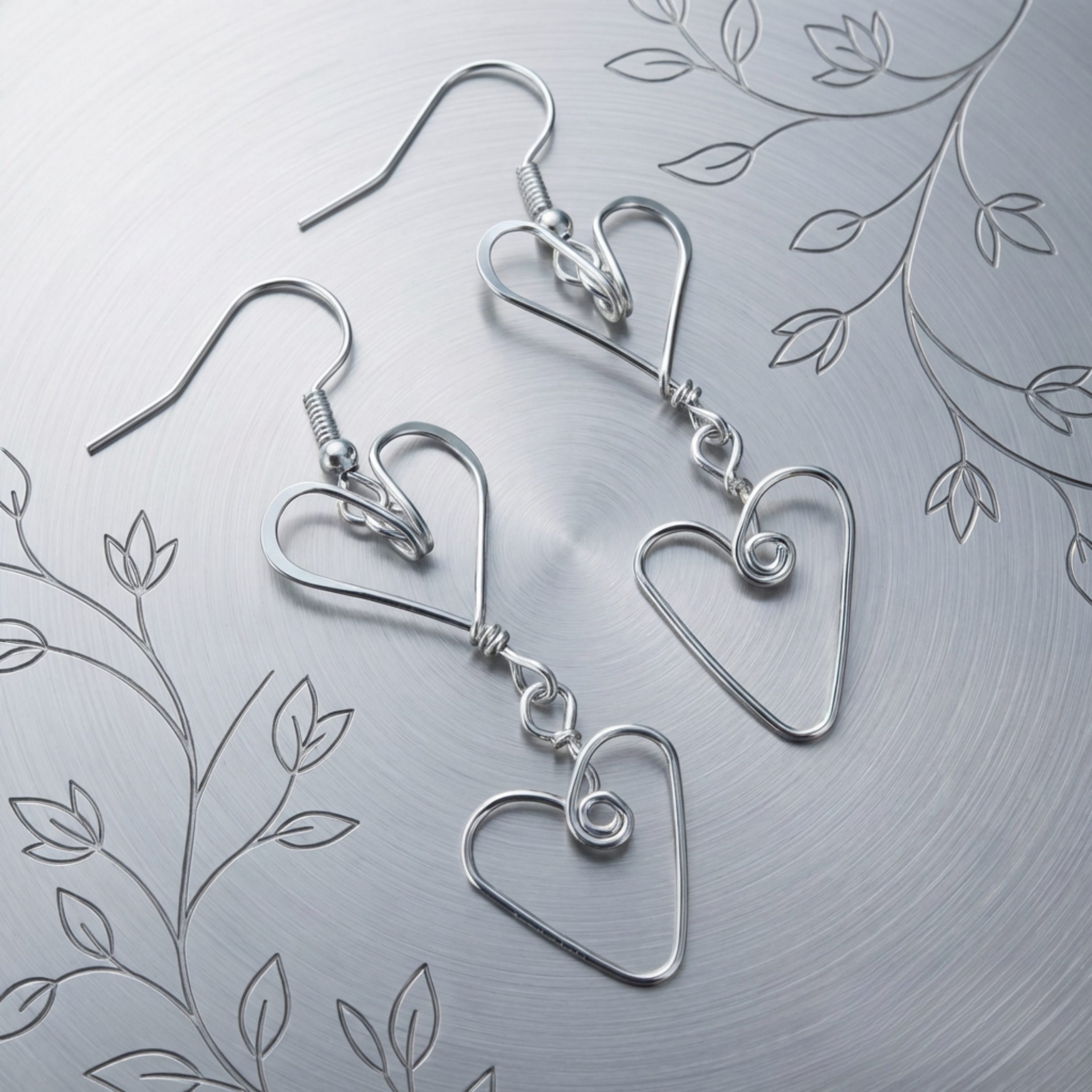 Silver heart-shaped earrings on a textured silver background with leaf patterns.