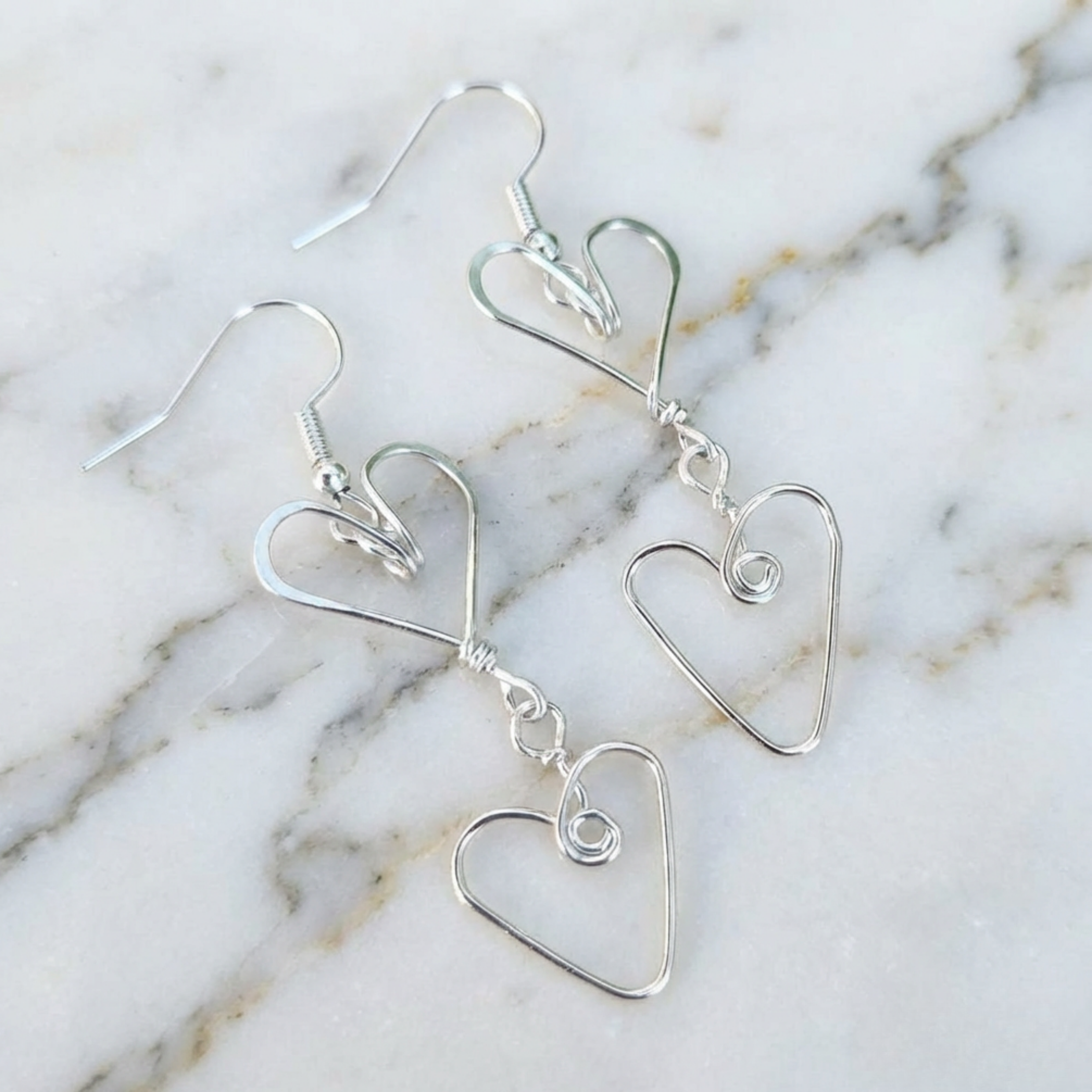 Silver heart-shaped earrings on a marble surface