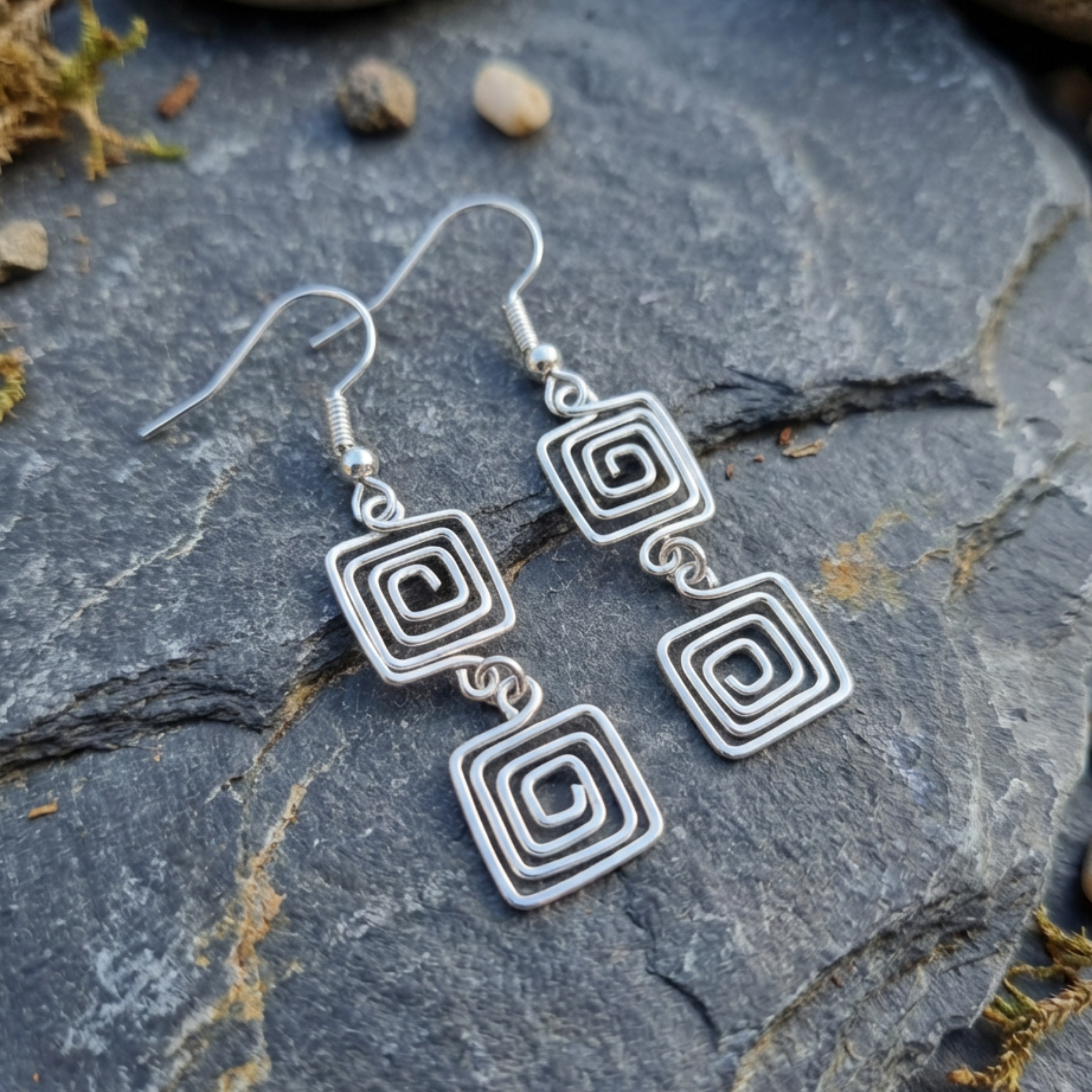 Silver spiral earrings on a stone surface