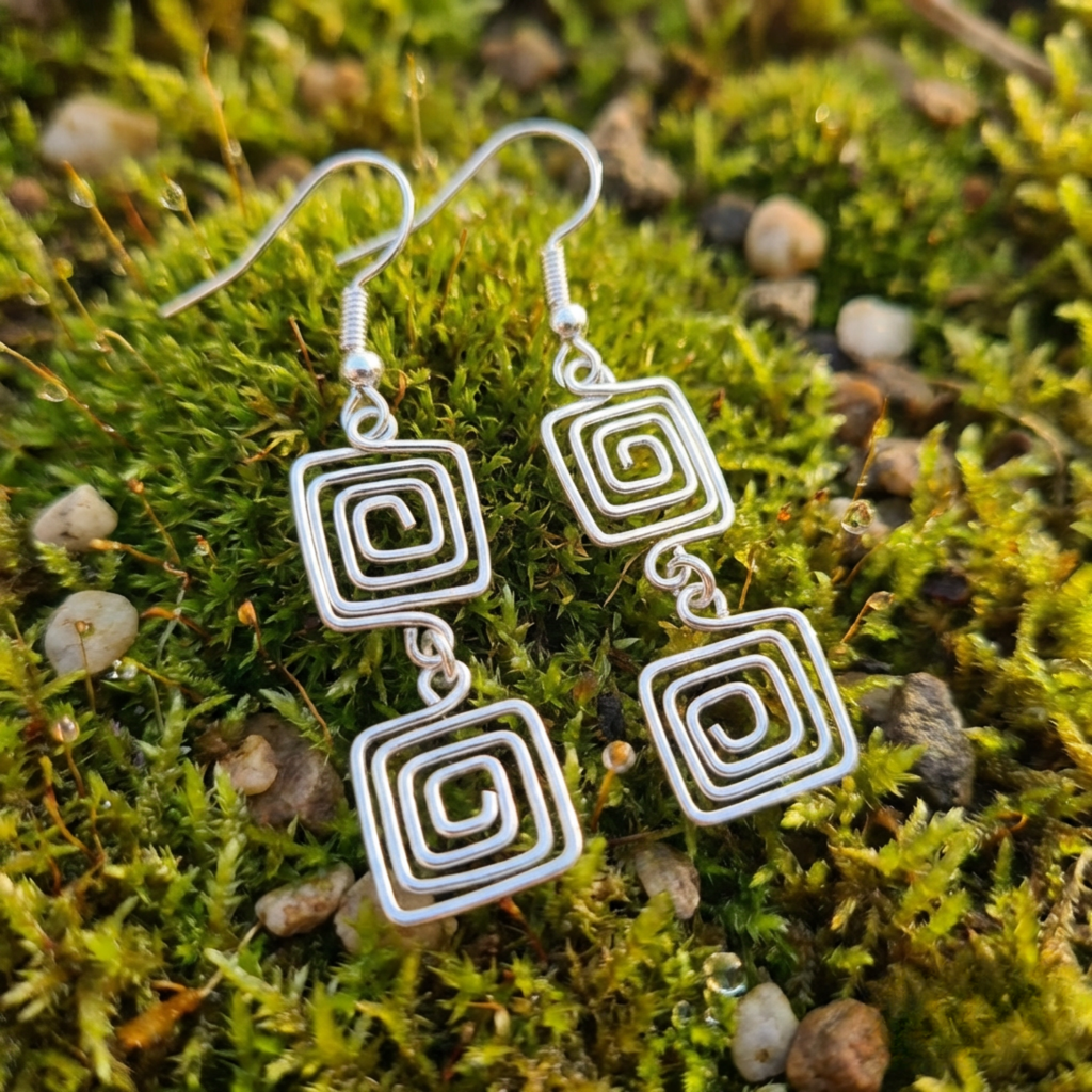 Silver spiral earrings on a natural background of green moss and small rocks.