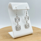 Silver square-patterned earrings on a white earring stand with a light gray background