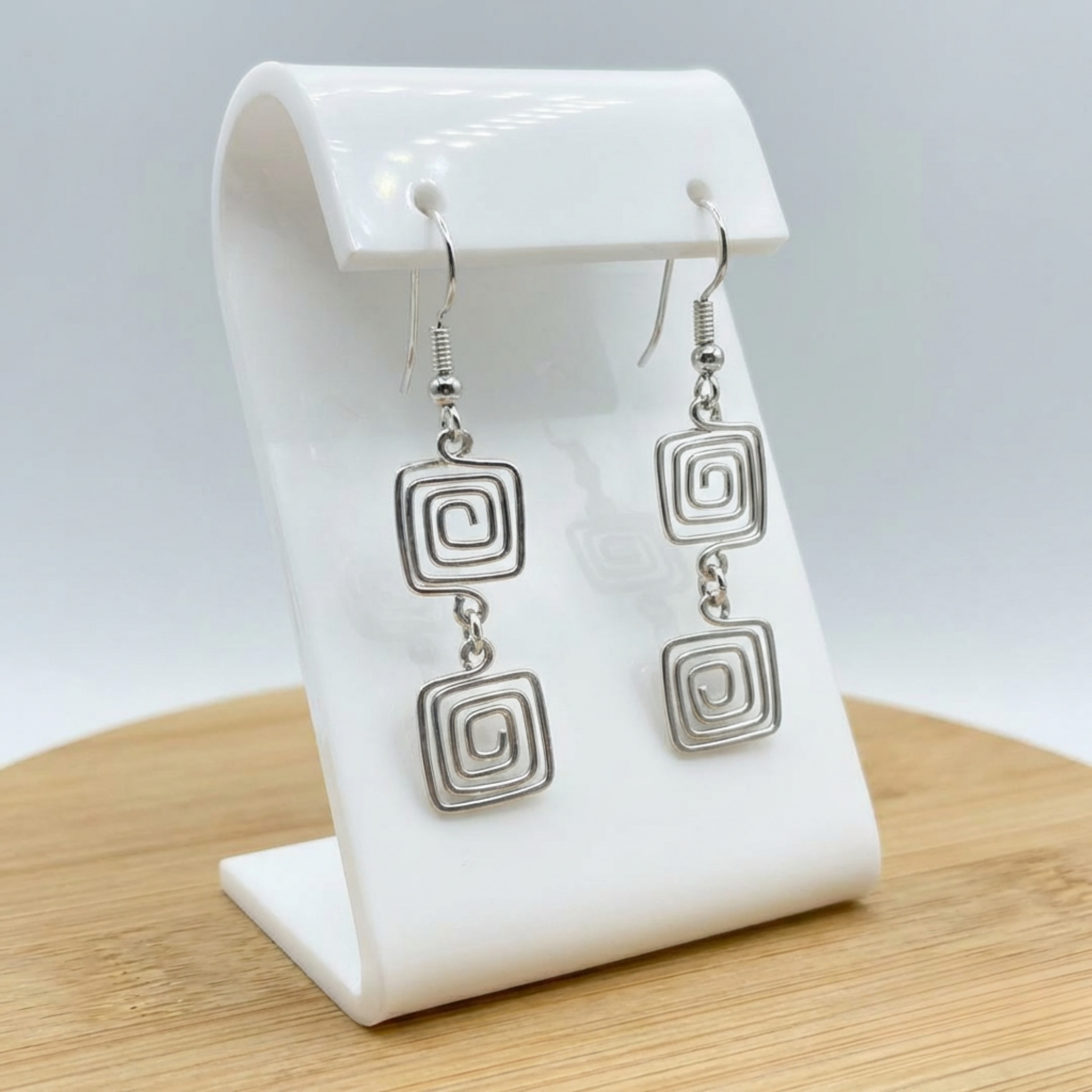 Silver square-patterned earrings on a white earring stand with a light gray background