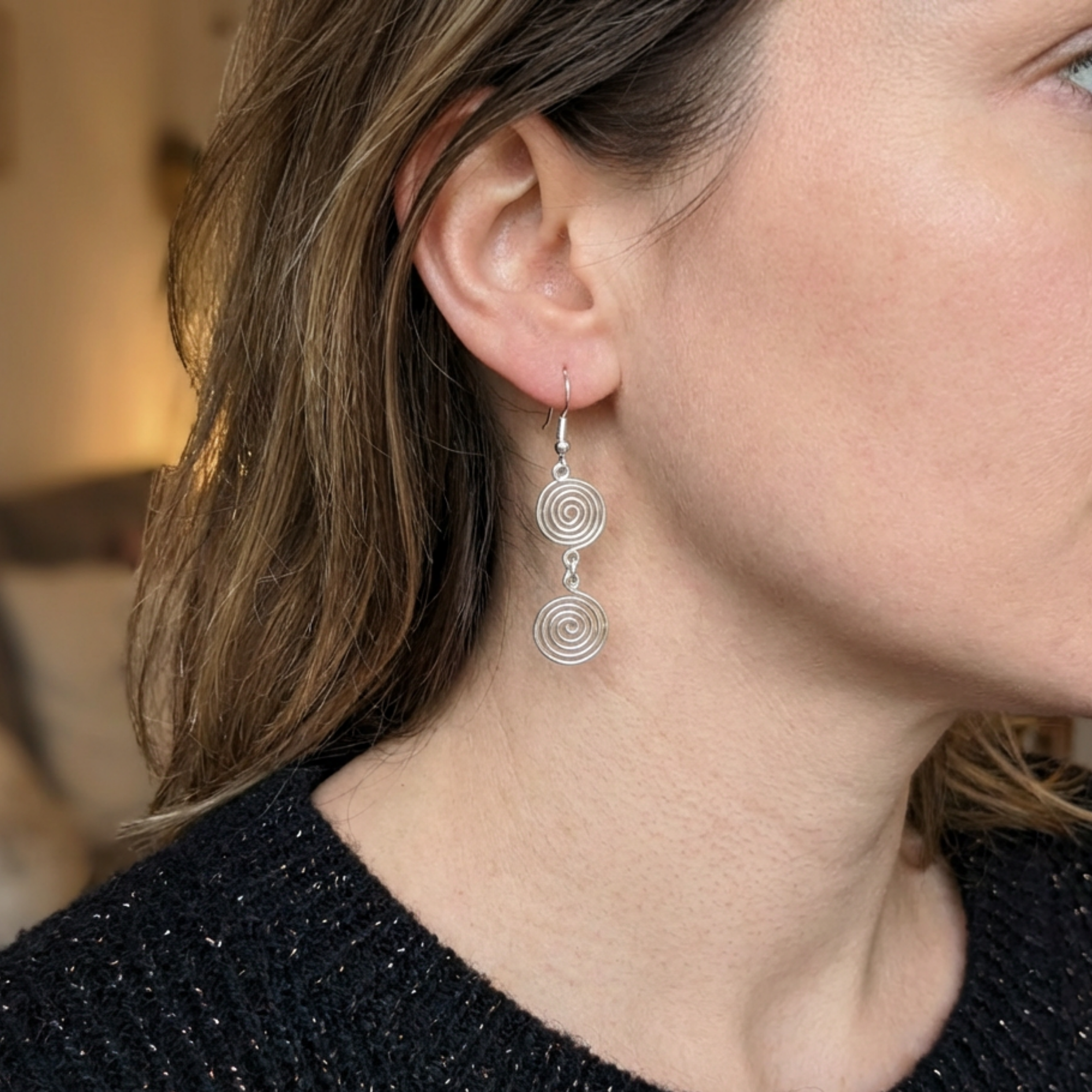 Close-up of a woman wearing silver spiral earrings with a blurred background