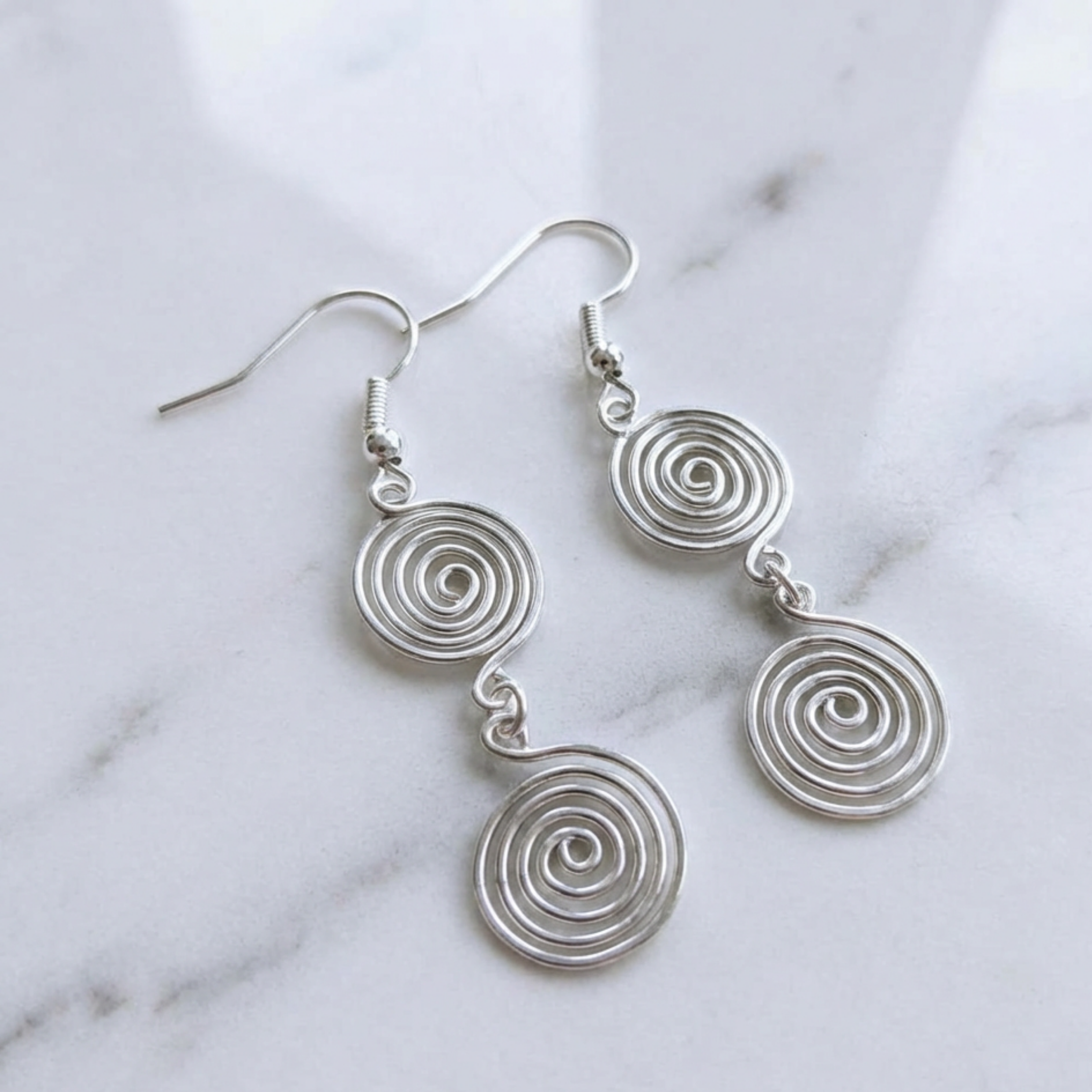 Silver spiral earrings on a marble background