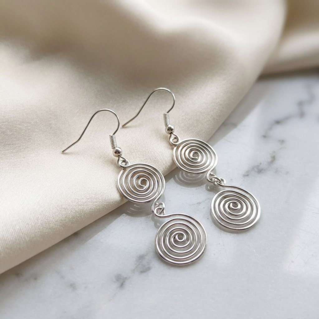 Silver spiral earrings on a marble surface with beige fabric background