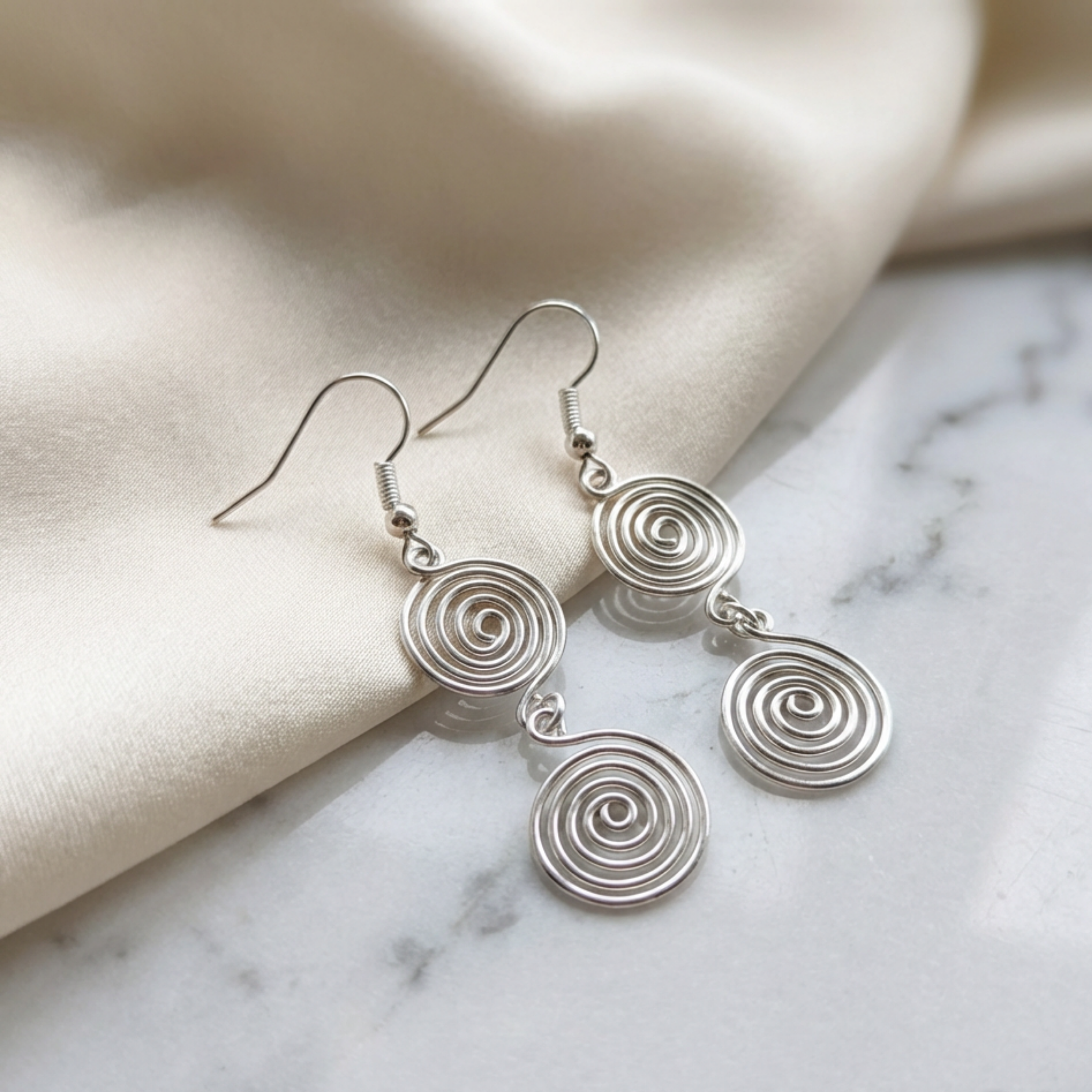 Silver spiral earrings on a marble surface with beige fabric background