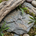 Silver spiral earrings on a stone surface with natural elements