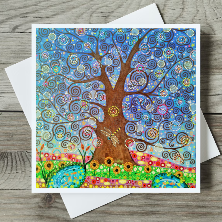 Colourful tree of life design with a dragonfly on a greeting card with white envelope on wooden surface