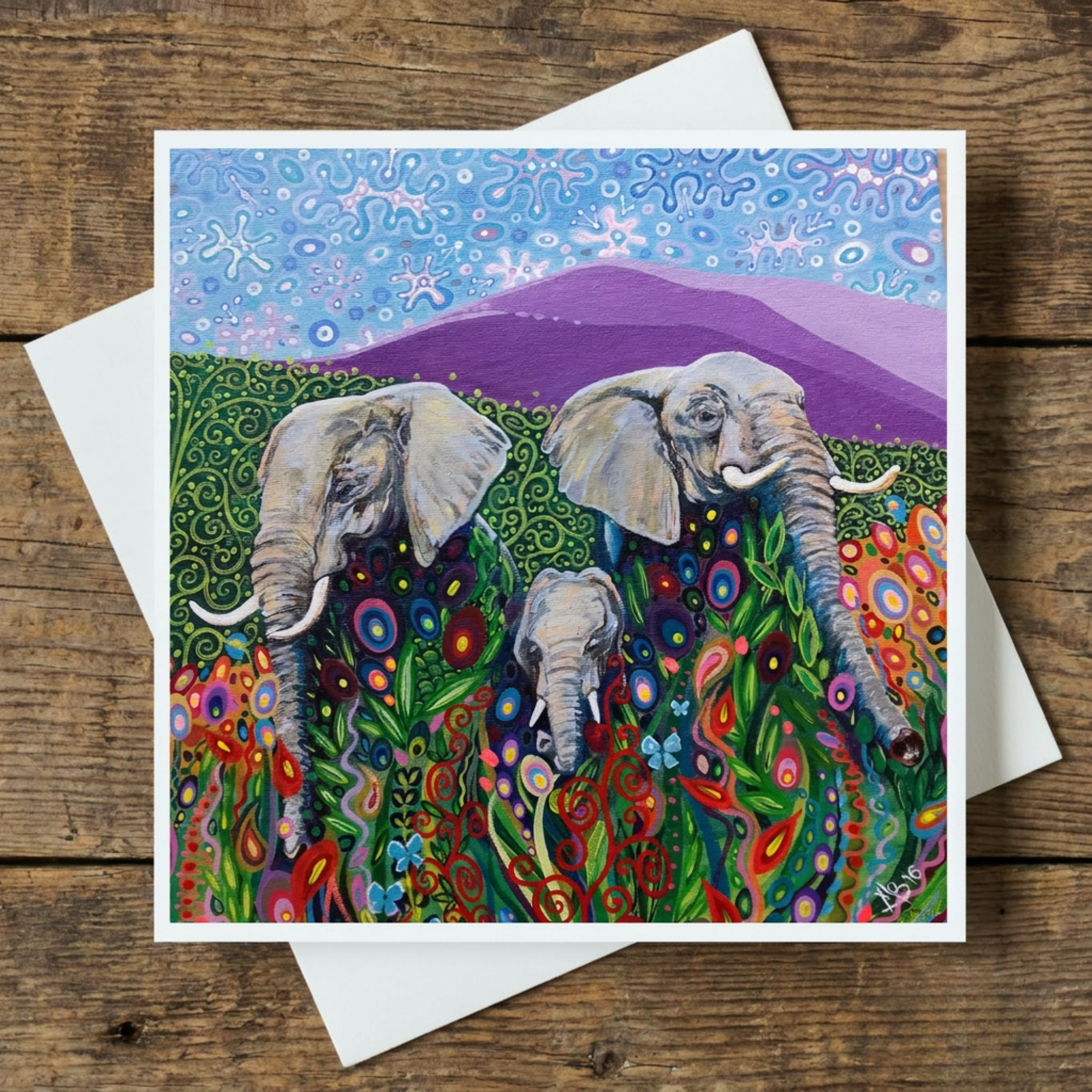 Elephant family in a colourful landscape greeting card on a wooden surface