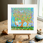 Colourful abstract artwork on a small easel with decorative stones on a wooden surface.
